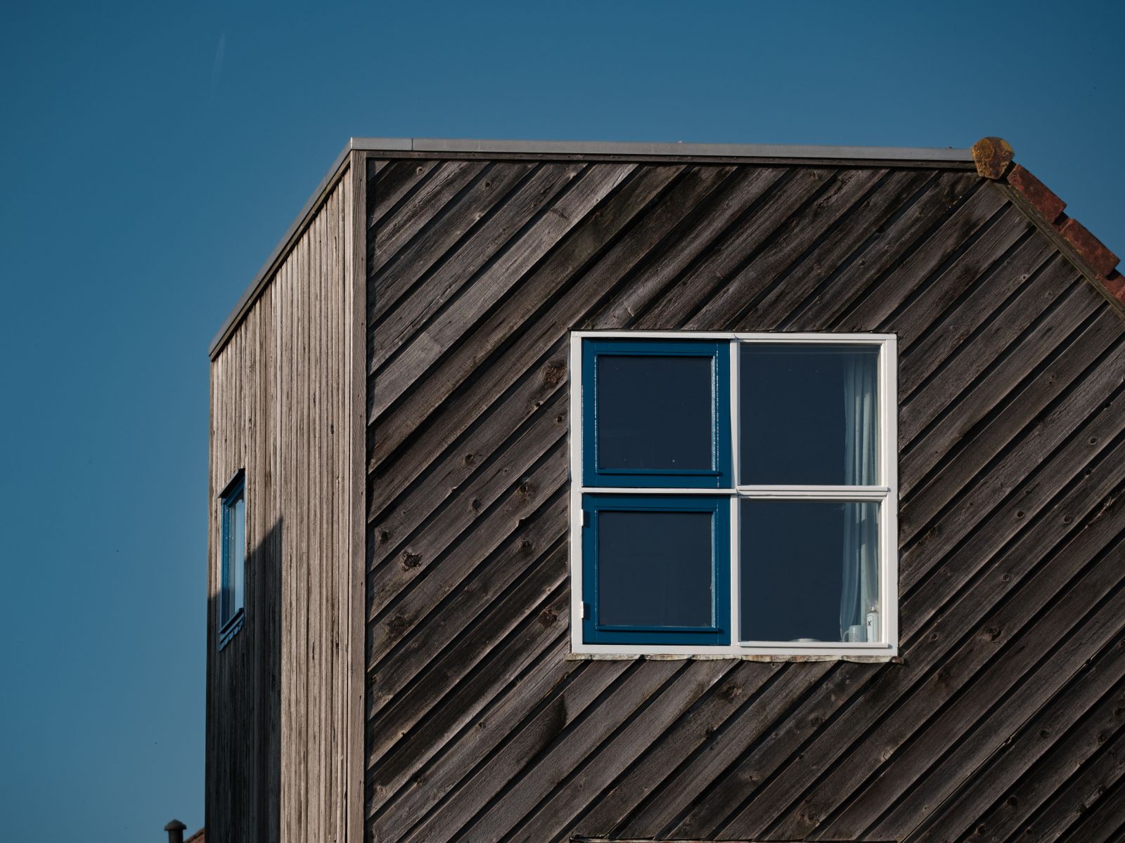 Väderbiten träfasad med diagonal panel och ett blått fönster — referensbild, inte ett Kult-bygge.