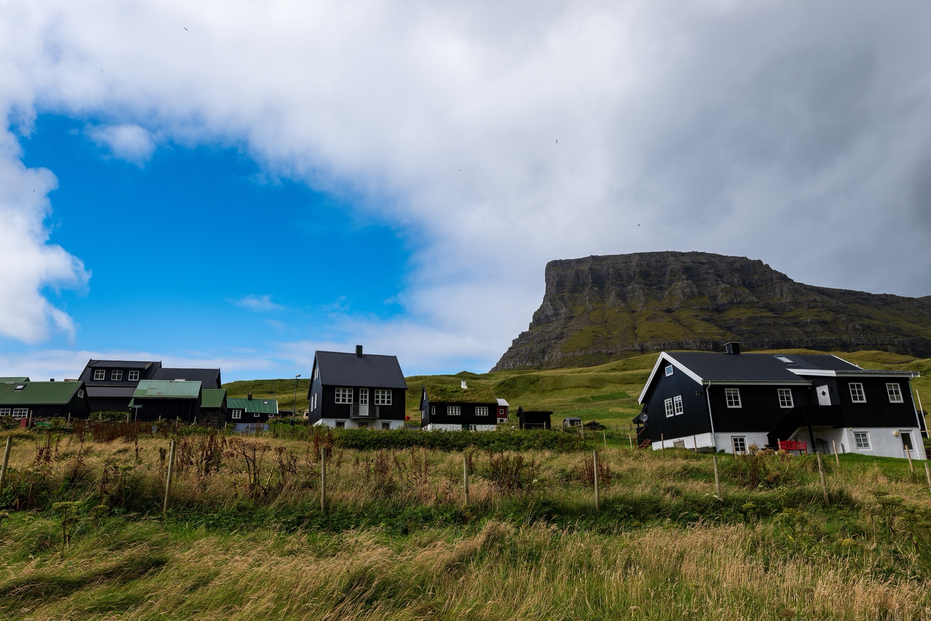 Svarta trähus i en by under ett brant fjäll — referensbild, inte ett Kult-bygge.